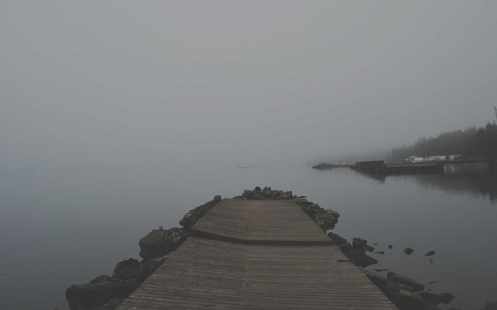 Muelle de piedra que se adentra en un agua quieta envuelta en niebla