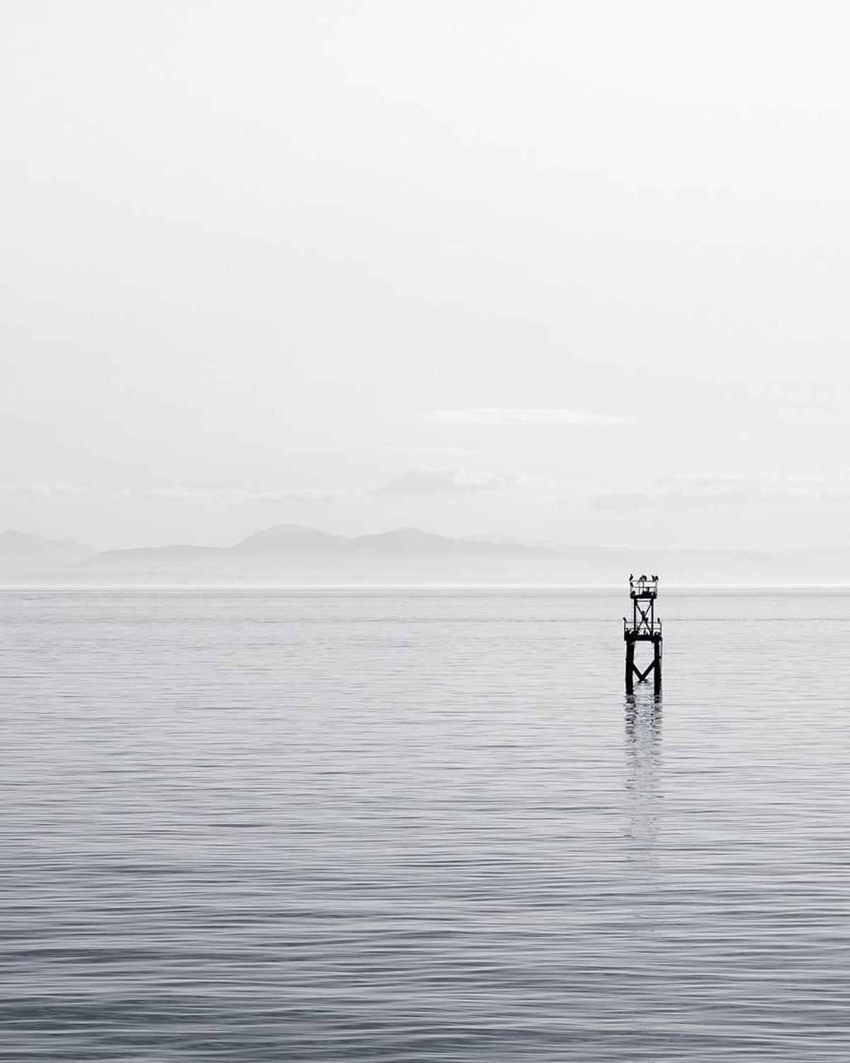 Un poste solitario en un agua en calma cubierta de niebla